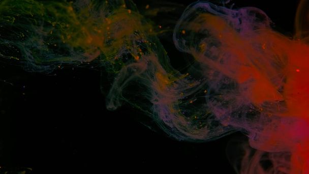 Drops of yellow, purple and orange ink in water. Yellow, purple and orange watercolor paints in water on a black background. Awesome abstract background. Beautiful wallpaper for your desktop. Colored cloud of ink on a black background. - Foto, imagen