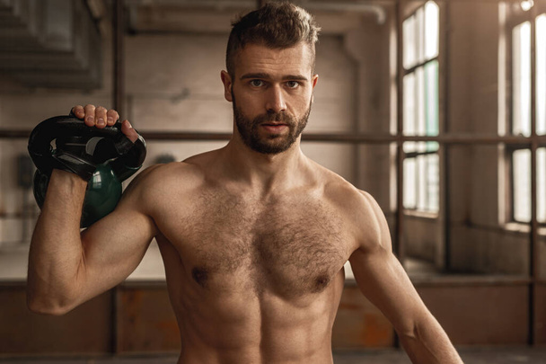 Strong muscular man lifting kettlebell in gym - Foto, afbeelding