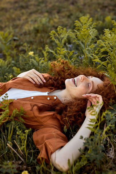 Positive happy lady is lying on green grass in forest field, romantic time in nature - Фото, изображение