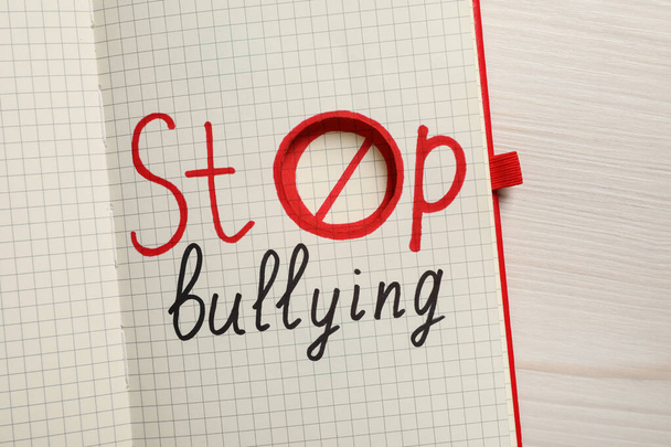 Open notebook with phrase Stop Bullying on white wooden table, top view - 写真・画像