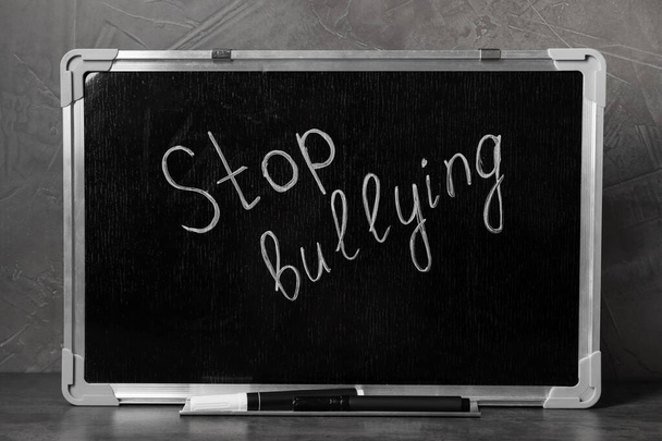 Chalkboard with phrase Stop Bullying on table near grey wall - Foto, Imagen