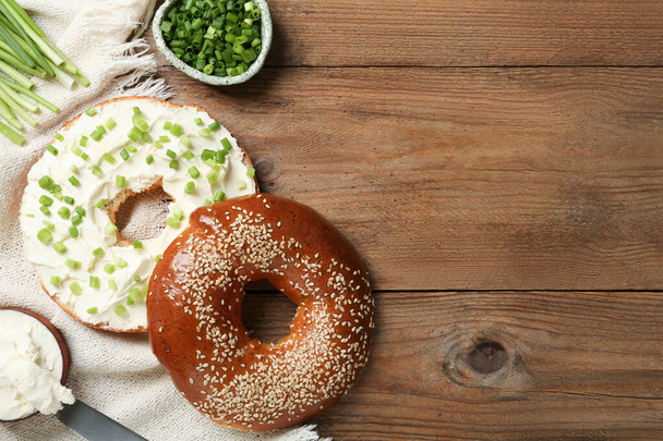 Delicious bagel with cream cheese and green onion on wooden table, flat lay. Space for text - Foto, immagini