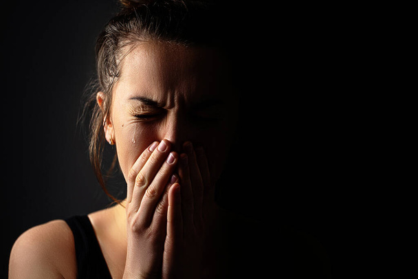 Sad grieving crying female with folded hands and tears eyes on a dark black background during trouble, life difficulties, loss and emotional problems. Copy space  - Foto, Bild