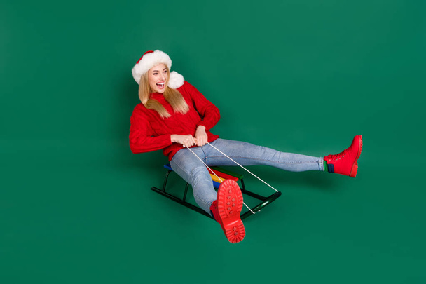 Portrait of attractive childish cheerful girl riding sledge having fun festive day good mood isolated over green color background - Valokuva, kuva