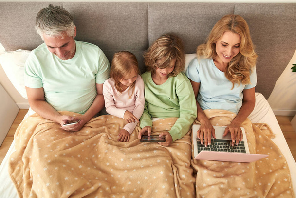 Happy family with kids stay in bed use devices - Zdjęcie, obraz