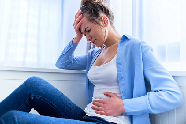 Sick painful woman suffering from stomach ache and strong spasm abdominal pain during gastric ulcer, appendicitis or gastrointestinal system disease, health problems - 写真・画像
