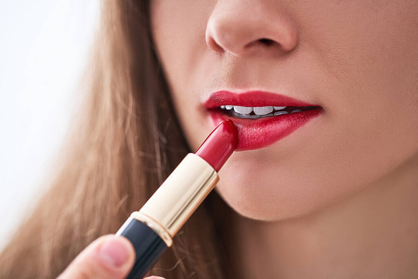 Female applying classic bright matte red lipstick on her lips close up - Foto, afbeelding