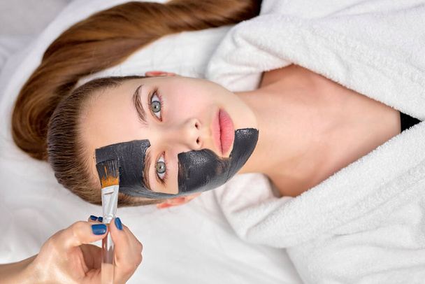 Top View on Young attractive woman in spa salon with black mask on face, copy space - Photo, Image