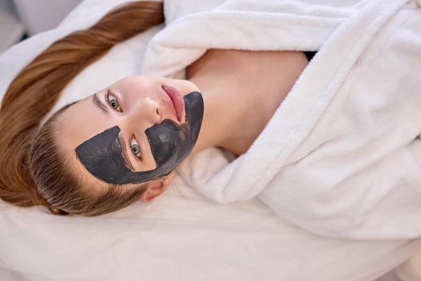 Top View On Good-looking Cute Female With Black Facial Mask on Half Of Face - Фото, изображение