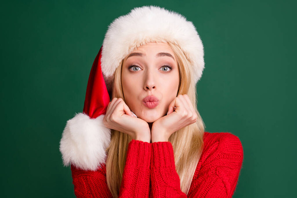 Photo of adorable dreamy young lady wear red sweater headwear sending you kiss arms cheeks chin isolated green color background - Foto, imagen