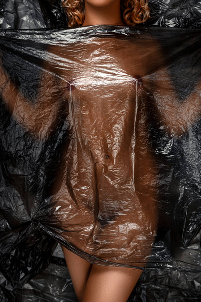Plastik torba giymiş genç bir Asyalı kızın çıplak vücudunun parçaları. Artistik bir tahılla rötuş yapılmış bir fotoğraf. Çevrenin plastik kirliliği sorunu. - Fotoğraf, Görsel
