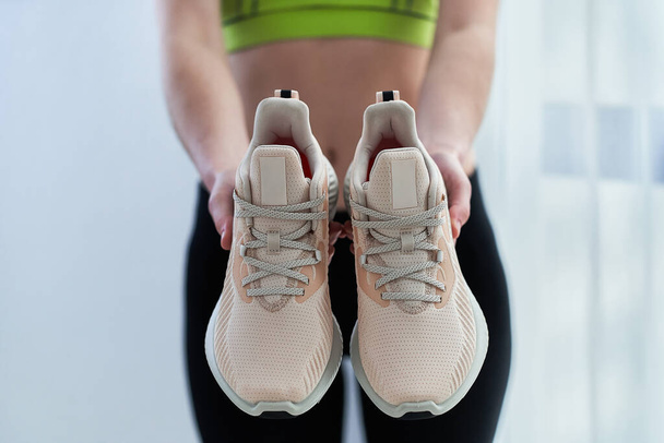 Athletic woman in sportswear holds beige sneakers for jogging and workout. Do sport and be fit. Sports people with healthy sporty lifestyle    - Fotografie, Obrázek