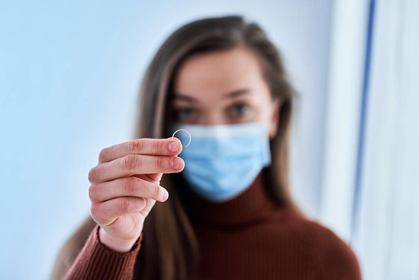Woman in protective mask holds ring. Break up marriage after living together and staying home with husband at quarantine and isolation due to coronavirus epidemic. Divorce concept  - Foto, Imagen