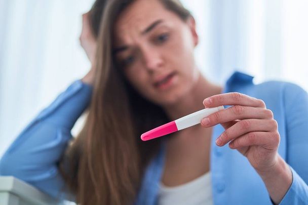 Shocked surprised woman holds pregnancy test with positive result. Unplanned and unwanted pregnancy - Photo, Image