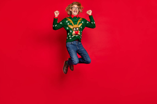 Photo of handsome funky young guy dressed print pullover jumping rising fists smiling isolated red color background - Photo, image