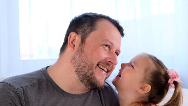 little joyful daughter, 3 years old, tells her dad a secret, play together at home. Fathers day. Handsome young man at home with his little cute girl are having fun together. Fatherhood concept - Valokuva, kuva