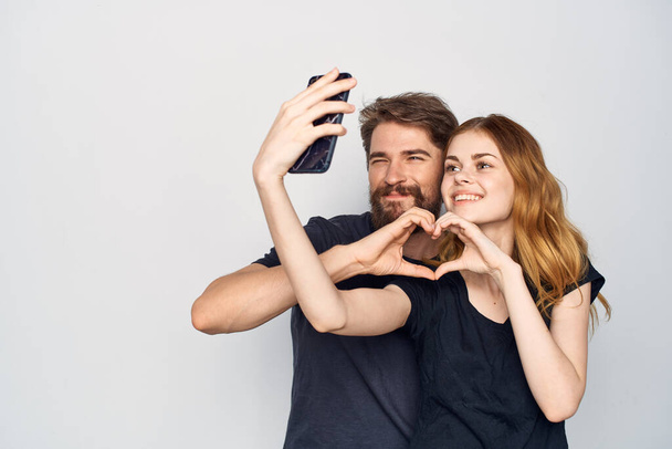 alegre joven pareja en negro camisetas teléfono divertido juntos amistad luz fondo - Foto, imagen