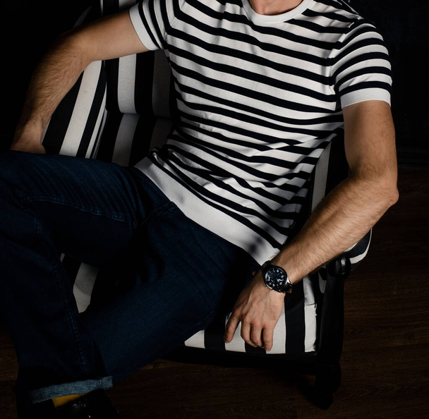 An unrecognizable man in a striped T-shirt sits on a striped armchair. - Фото, изображение
