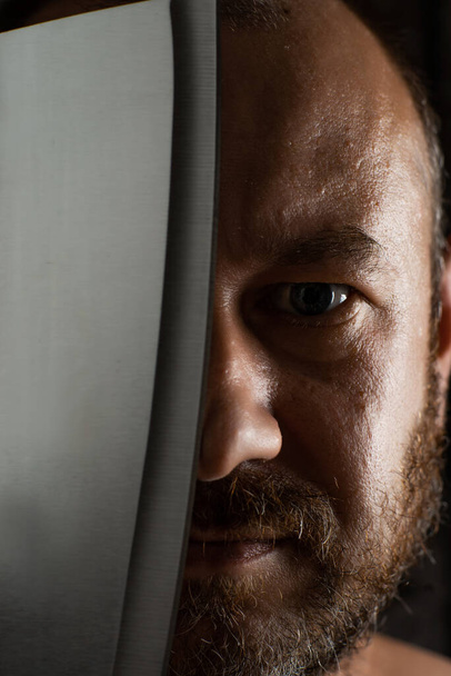 Unshaven middle-aged man with a butcher knife close-up. - Фото, изображение