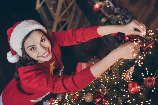 Photo of funky adorable young woman dressed print pullover headwear decorating christmas tree smiling indoors room home house - 写真・画像