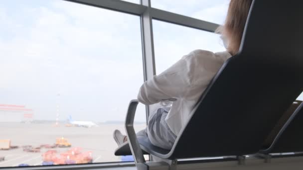 Mulher descansa em uma cadeira no terminal do aeroporto e espera por avião de trânsito - Filmagem, Vídeo