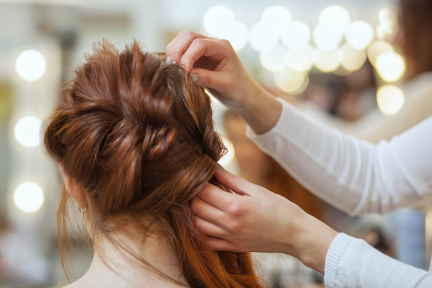 Красивая, с длинными рыжими волосатыми девочками, парикмахер плетёт французскую косу в салоне красоты. Профессиональный уход за волосами
. - Фото, изображение