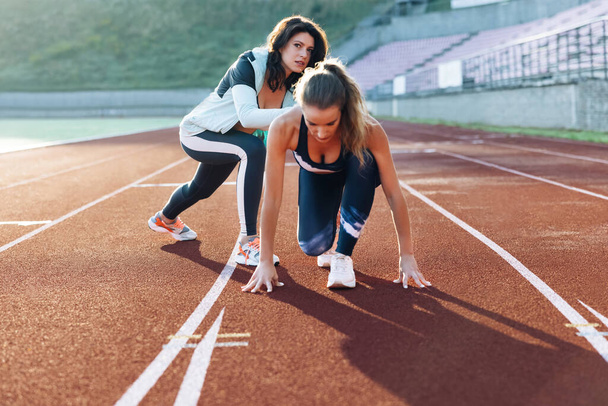 Young athlete exercises with personal trainer standing on start on stadium, then rushing forward, getting ready for competition. Female athlete on track. Exercising strength, cardio and power. - Foto, imagen
