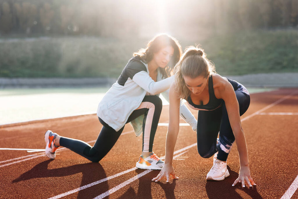 Caucasian Athlete ready to start. Young female runner with personal trainer preparing for blasting off in mist on sports track of stadium, training before competition. Sportswoman. Cardio exercises - Photo, image