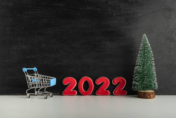 Christmas tree, trolley cart and numbers 2022 on light background. Shopping for the New year. Copy space. - Photo, Image