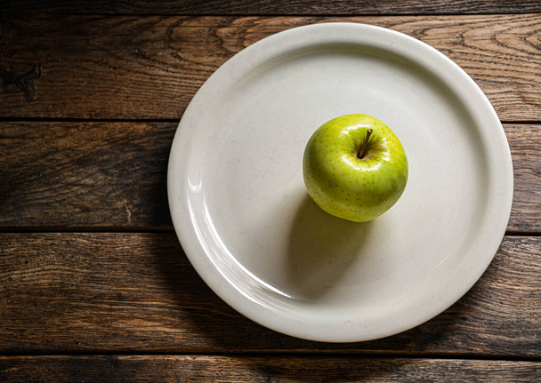 One green apple on a white ceramic plate, on a wooden table. - Photo, Image