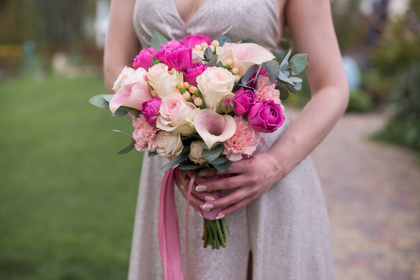 Um lindo buquê nupcial de rosas rosa e creme, cravos em pó e lírios de calla delicados nas mãos da noiva. - Foto, Imagem