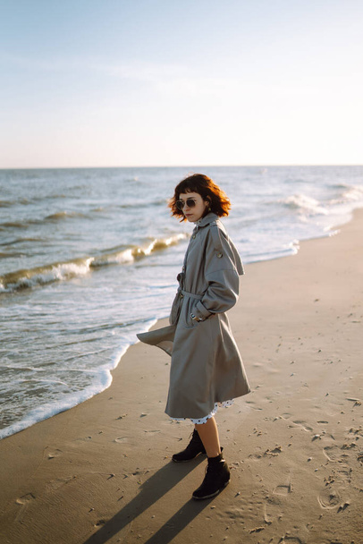 Stylish woman in fashionable clothes walks along seashore during autumn sunny day. Travel, weekend, relax and lifestyle concept.  - Fotografie, Obrázek