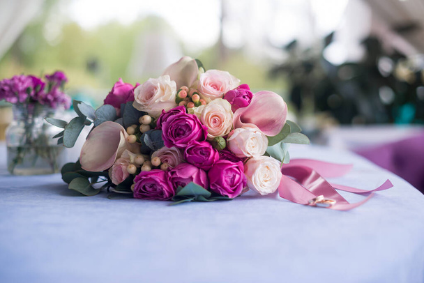 Un hermoso ramo nupcial de rosas rosadas y crema, claveles en polvo y delicados lirios de calas se encuentra sobre la mesa. - Foto, Imagen