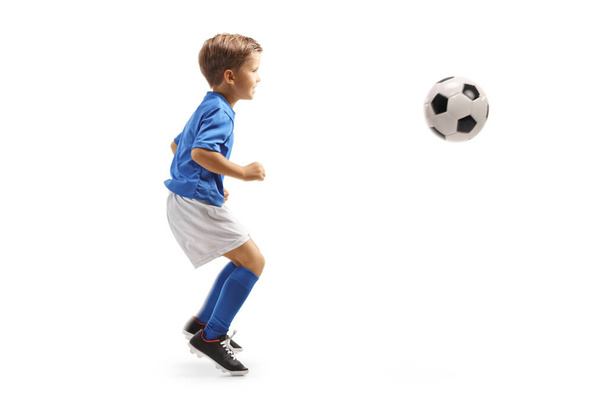 Full length profile shot of a little boy jumping with a soccer ball isolated on white background - Fotó, kép
