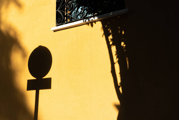 Sombra de cartel de trafico y arbol ayık Amarilla con ventana / Trafik işaretinin gölgesi ve pencereli sarı duvardaki ağaç  - Fotoğraf, Görsel