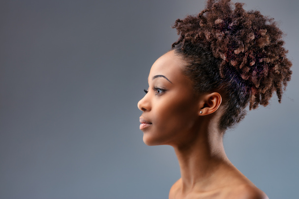 Mooie sexy jong zwart vrouw poseren met blote schouders kijken naar de kant richting copyspace op een blauwe studio achtergrond in close-up - Foto, afbeelding