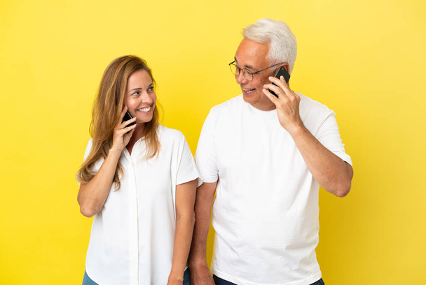 Ζευγάρι μέσης ηλικίας απομονωμένο σε κίτρινο φόντο μιλώντας σε κινητό - Φωτογραφία, εικόνα