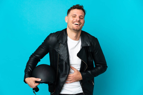 Caucasian man with a motorcycle helmet isolated on blue background smiling a lot - Photo, Image