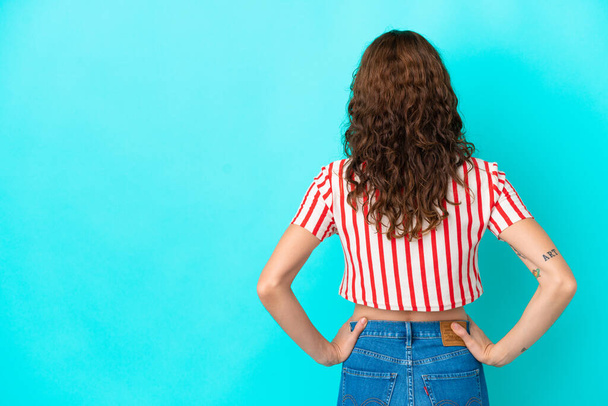 Young woman with curly hair isolated on blue background in back position - Foto, Imagem