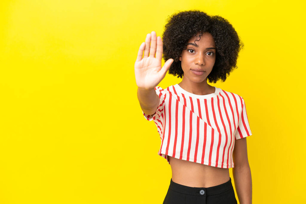 Молода афро-американська жінка ізольована на жовтому фоні робить стоп жест - Фото, зображення