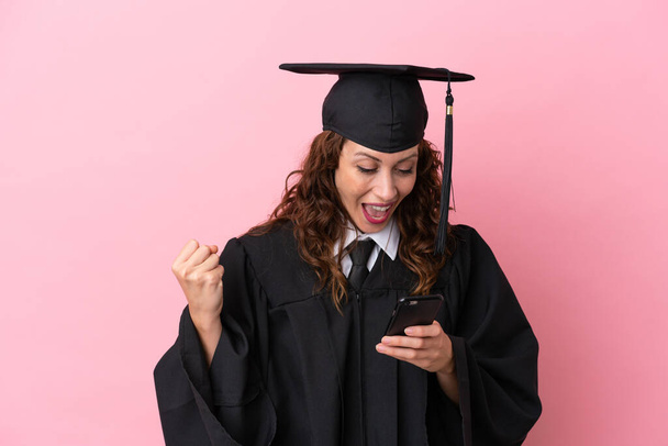 Young university graduate woman isolated on pink background surprised and sending a message - Foto, Imagen