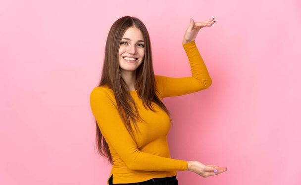 Young caucasian woman isolated on pink background holding copyspace to insert an ad - Fotoğraf, Görsel