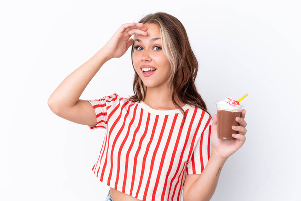 Mladá ruská dívka drží cappuccino izolované na bílém pozadí dělá překvapení gesto při pohledu na stranu - Fotografie, Obrázek
