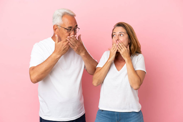 Μεσήλικες ζευγάρι απομονώνονται σε ροζ φόντο που καλύπτει το στόμα με τα χέρια - Φωτογραφία, εικόνα