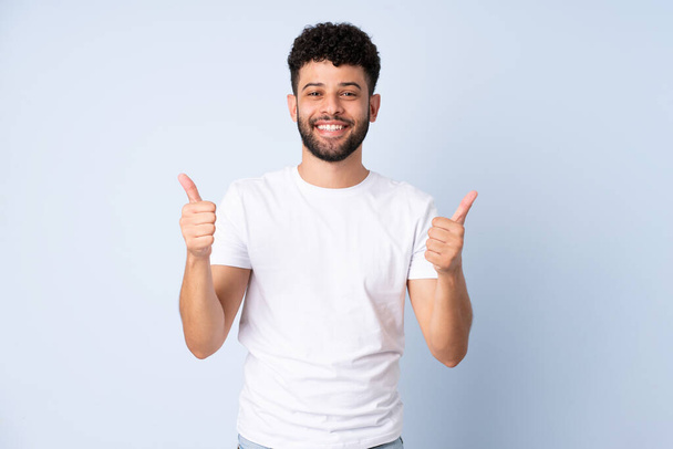Young Moroccan man isolated on blue background with thumbs up gesture and smiling - Photo, Image