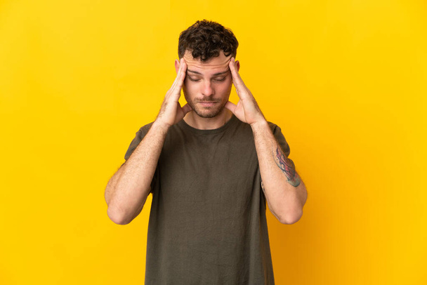 Young caucasian handsome man isolated on yellow background with headache - Fotó, kép
