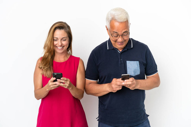 Střední věk pár izolované na bílém pozadí Překvapen a odeslání zprávy nebo e-mail s mobilem - Fotografie, Obrázek