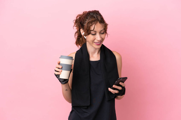 Sport sport woman with towel isolated on pink background holding coffee to take away and a mobile - Fotó, kép