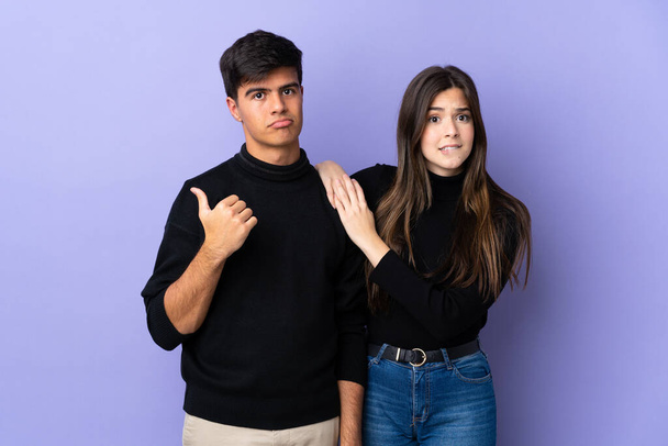 Young couple over isolated purple background frustrated and pointing finger to the side - Fotografie, Obrázek