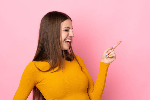 Young caucasian woman isolated on pink background pointing finger to the side and presenting a product - 写真・画像